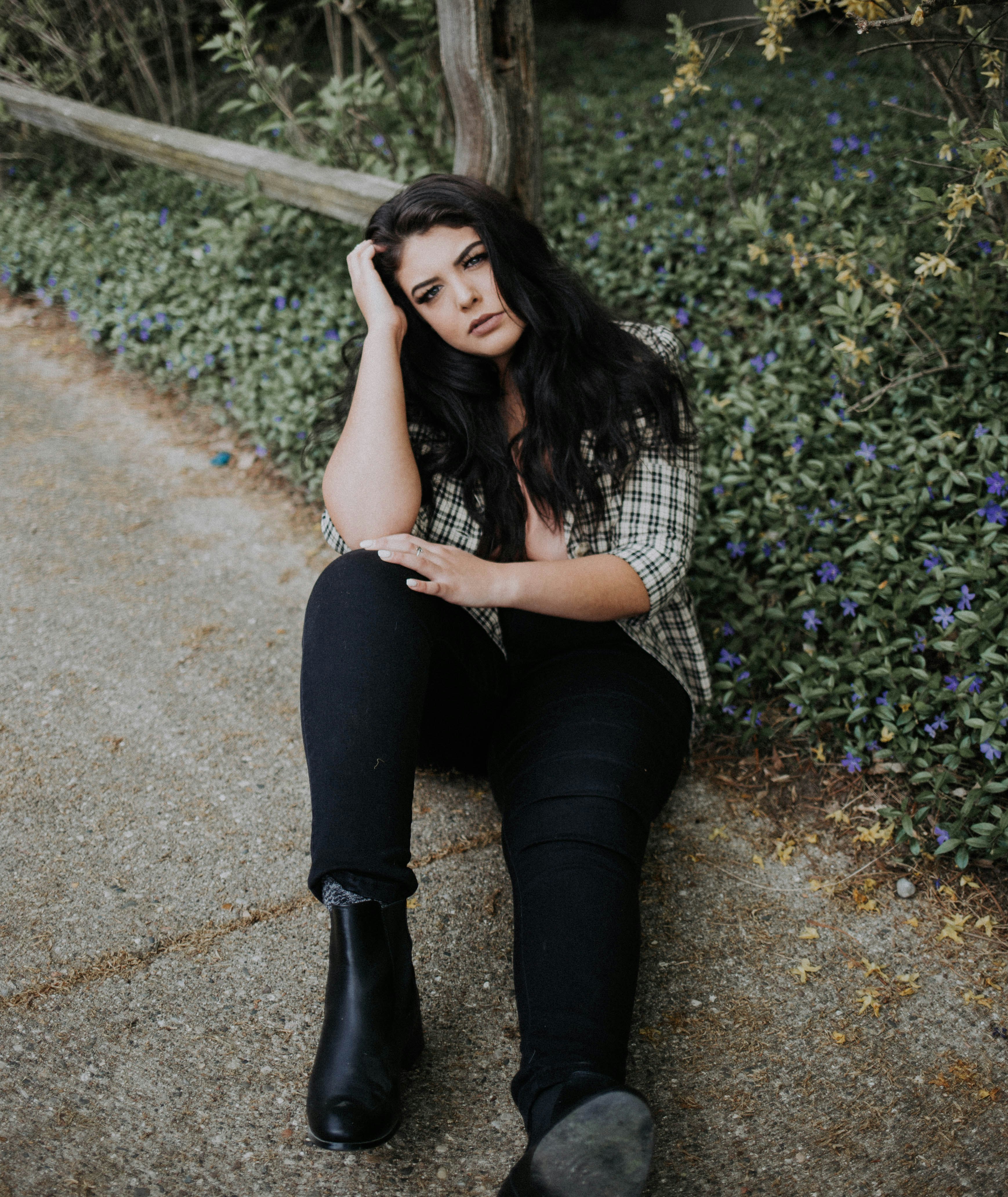 woman sitting on concrete pathway holding her head near green leaf plant